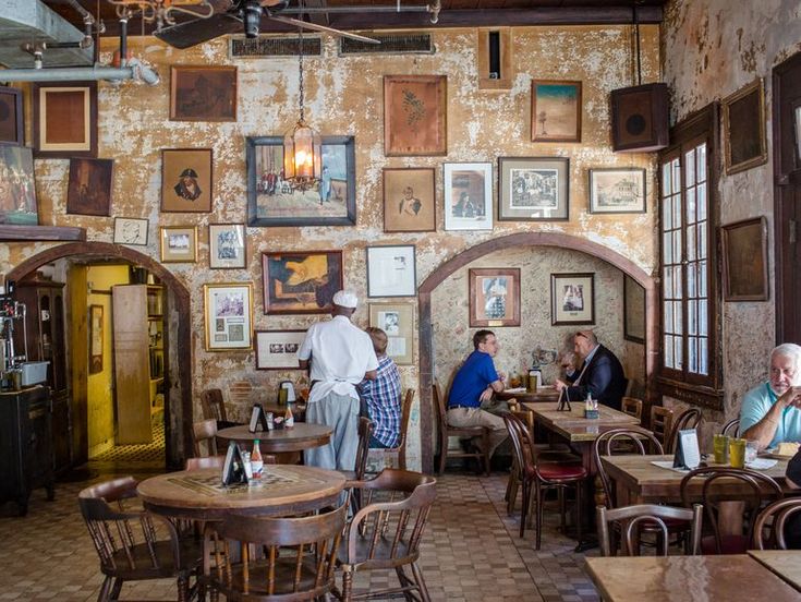 people sitting at tables in a restaurant with many pictures on the wall and windows above them