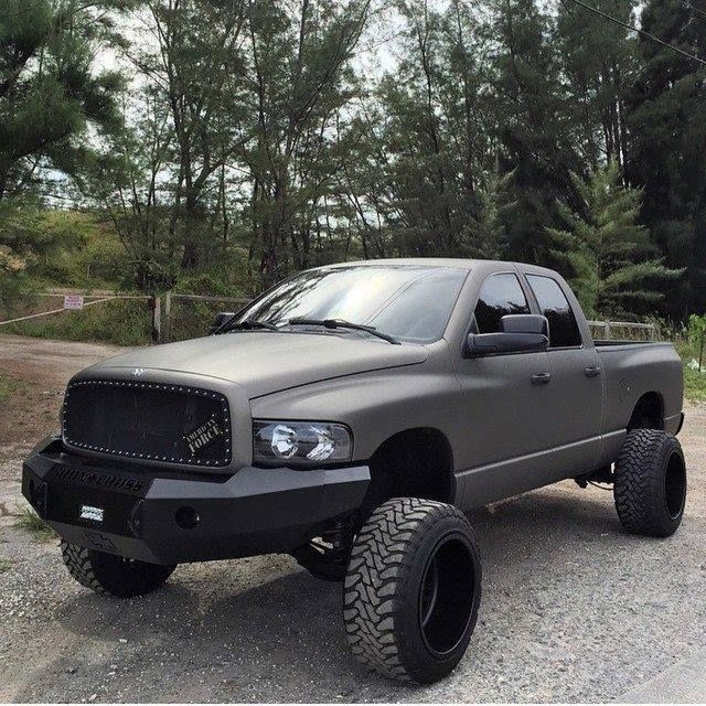 a large gray truck parked on top of a gravel road in front of some trees