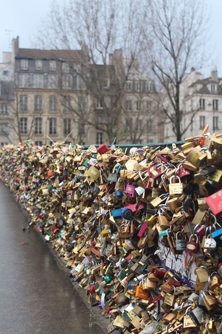 many padlocks are attached to the fence in front of some buildings and trees