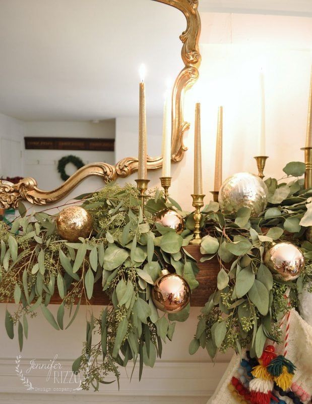 a mantle decorated with greenery, candles and gold ornaments in front of a mirror