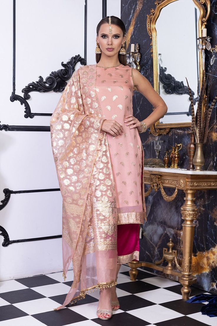 Siren This peach and magenta is a made in heaven combo. The depth of magenta perfectly settles in with the brightness of peach. The pure chiffon shirt in jacquard self-embroidery famously known as Banarasi embroidery. The fabric has a nice fall making extremely elegant. Paired up with silk magenta trouser with zarri patched border, Siren surely races up the heartbeats of everyone around. Matched with a jacquard design dupatta with pearl scallops -this outfit is a must-have for your wedding and festive wardrobe. It's an element of beauty that speaks itself. Top: Color: Peach Fabric: Pure chiffon Long shirt with zari motifs all over Closed neckline with gold pearls Sleeveless with gold pearls Bottom: Color: Magenta Fabric: Silk Zari patch on border Flared cropped pants Half elasticated waist Pink Sleeveless Traditional Wear With Resham Embroidery, Pink Silk Kurta With Chikankari Embroidery, Elegant Peach Kurta With Resham Embroidery, Designer Silk Pink Kurta, Designer Pink Silk Kurta, Elegant Peach Chanderi Kurta, Elegant Peach Chanderi Dupatta, Elegant Peach Kurta With Zari Work, Elegant Peach Kurta With Dupatta