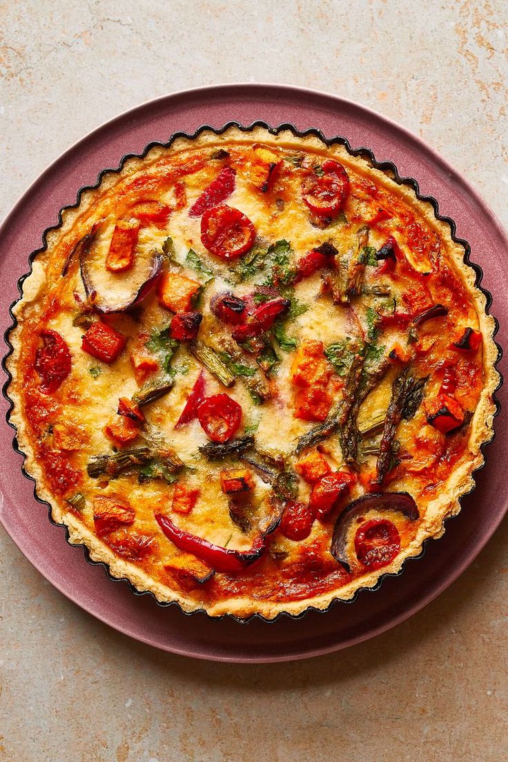 a quiche with tomatoes and asparagus is on a purple plate, ready to be eaten