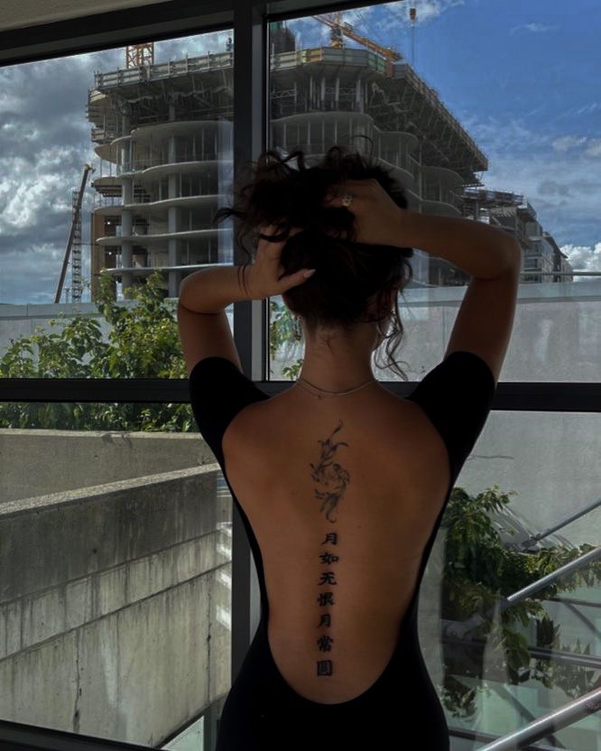 the back of a woman's body with chinese writing on her left side and an ocean in the background