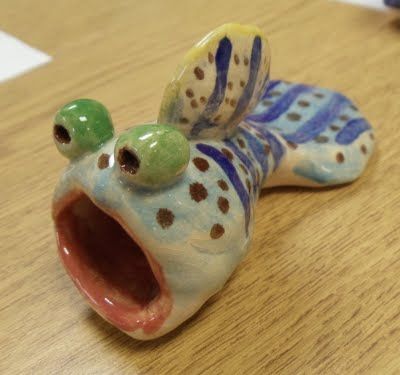 a ceramic frog figurine with its mouth open and eyes wide open on a wooden table