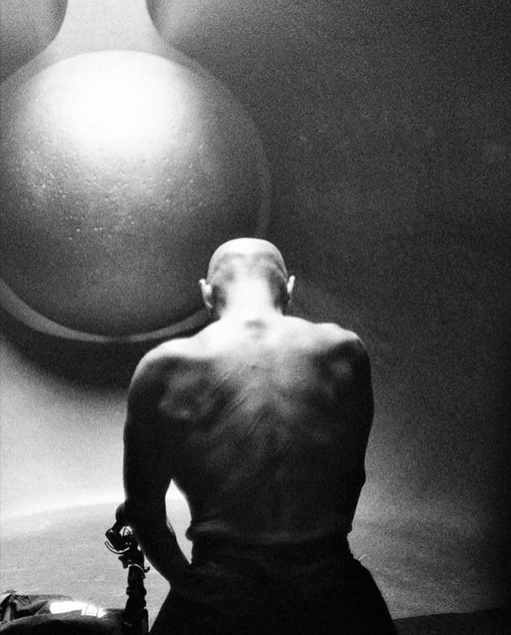 black and white photograph of a man sitting in front of a large sphere on the wall