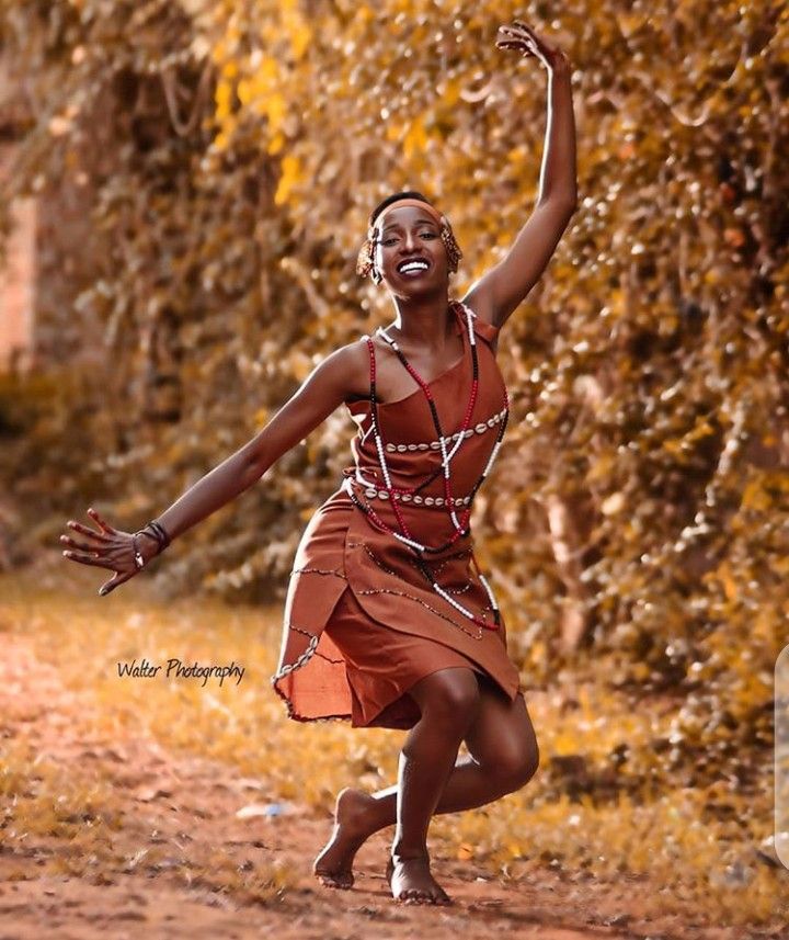 a woman in an orange dress is playing with a frisbee on a dirt road