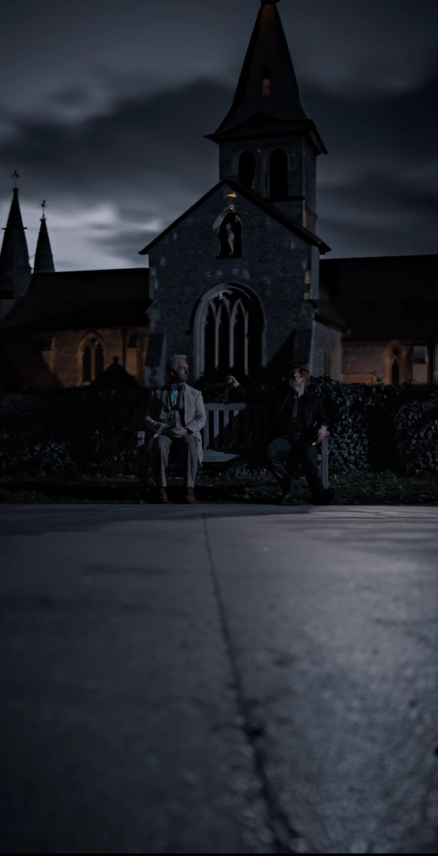 two people sitting on a bench in front of a church at night with the moon behind them