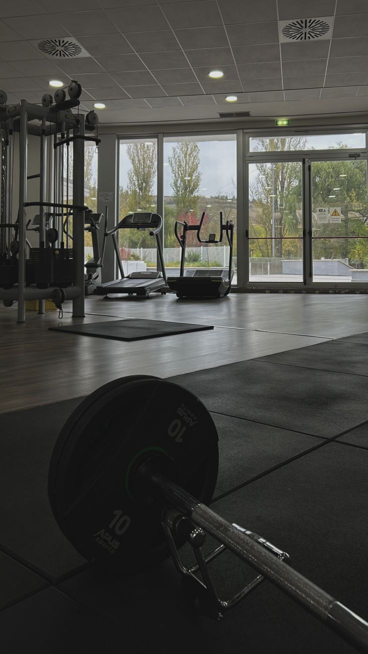 an empty gym with exercise equipment in the foreground and large windows on the other side