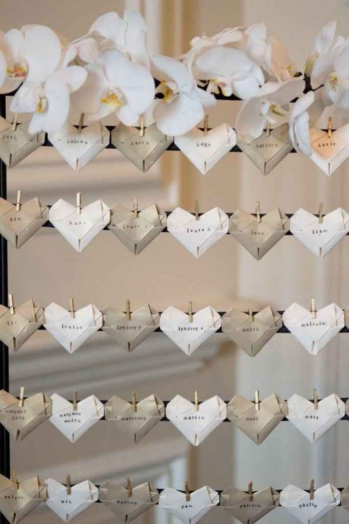 there are many hearts hanging on the wall with name tags attached to them and some flowers in front of it