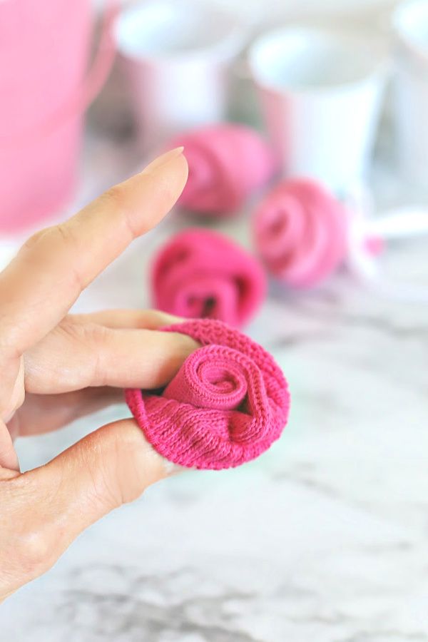 a hand holding a piece of pink crocheted fabric in the shape of a flower