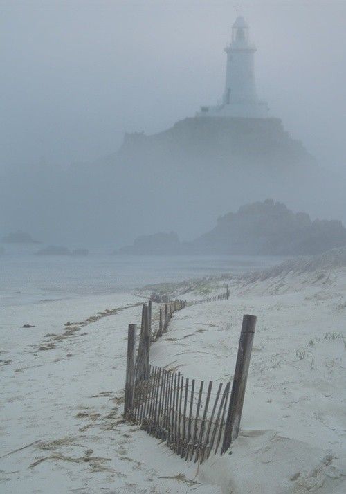 a foggy beach with a fence and lighthouse in the background