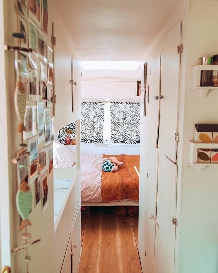 a narrow hallway leading to a bedroom with a bed and pictures on the wall above it