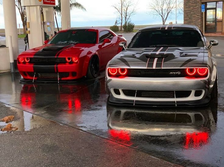 two cars parked next to each other at a gas station on a rainy day with red lights