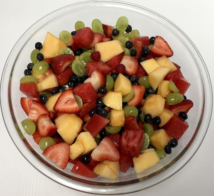 a glass bowl filled with fruit salad on top of a white table