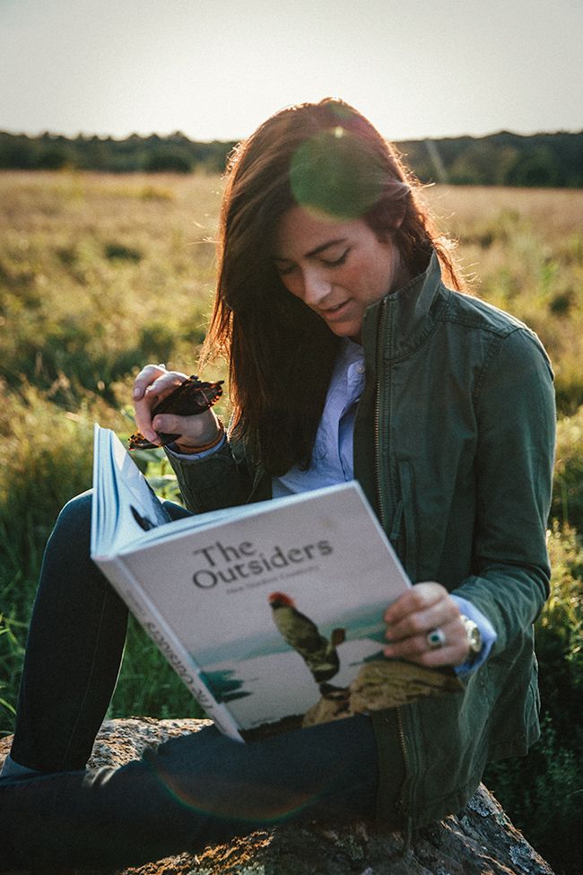 a woman sitting on a rock reading a book