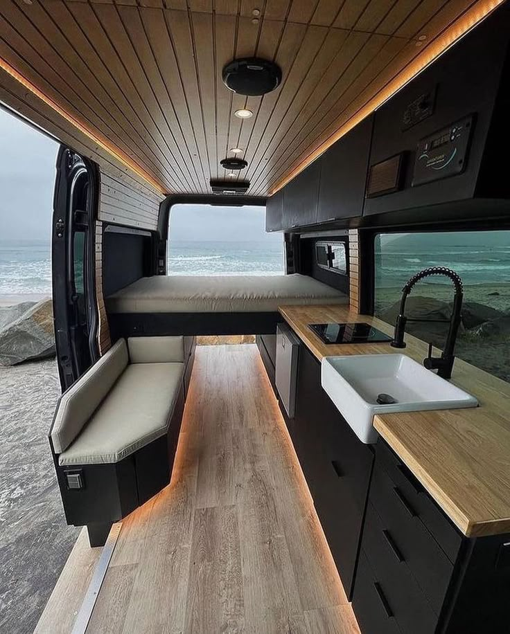 the interior of a camper with wood flooring and black cabinets, along with an open kitchen area