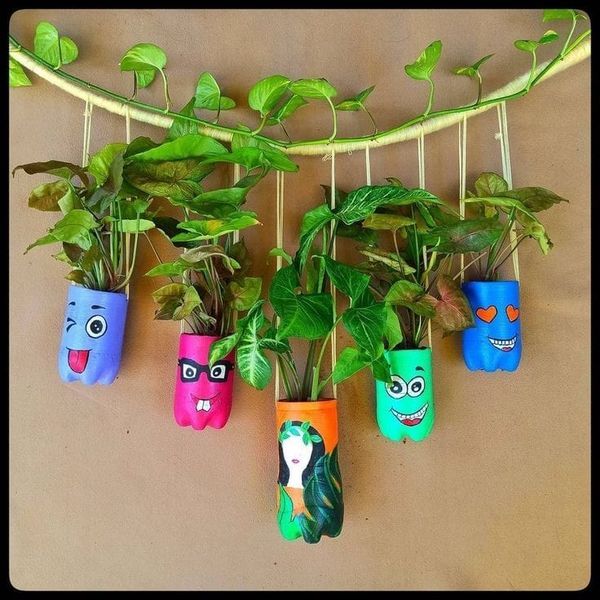 some plants that are hanging on the wall and have faces painted on their pots in them