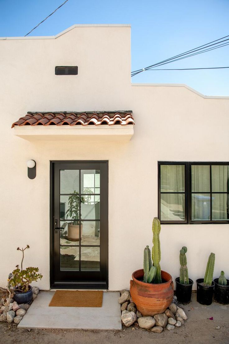 a white house with a cactus in front of it and two potted cacti next to the door