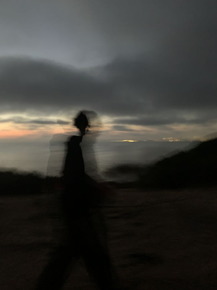 a blurry image of a person walking on a hill at dusk with the sun setting in the distance