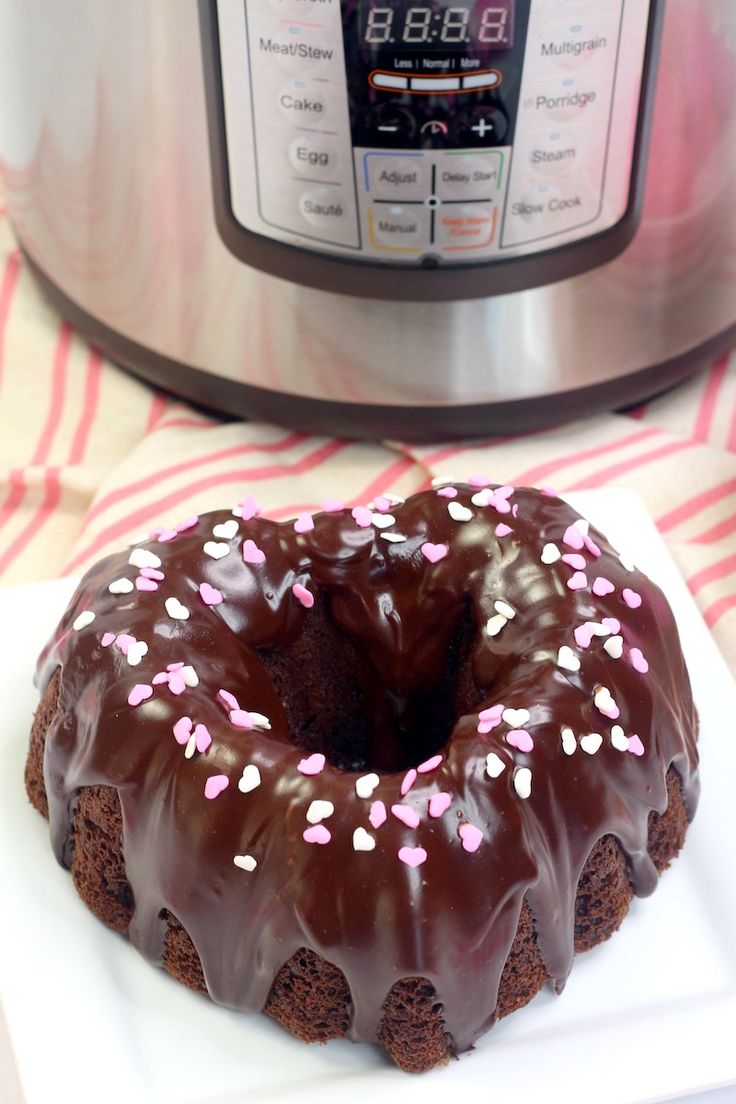 a chocolate bundt cake with pink sprinkles on a white plate in front of an instant pressure cooker