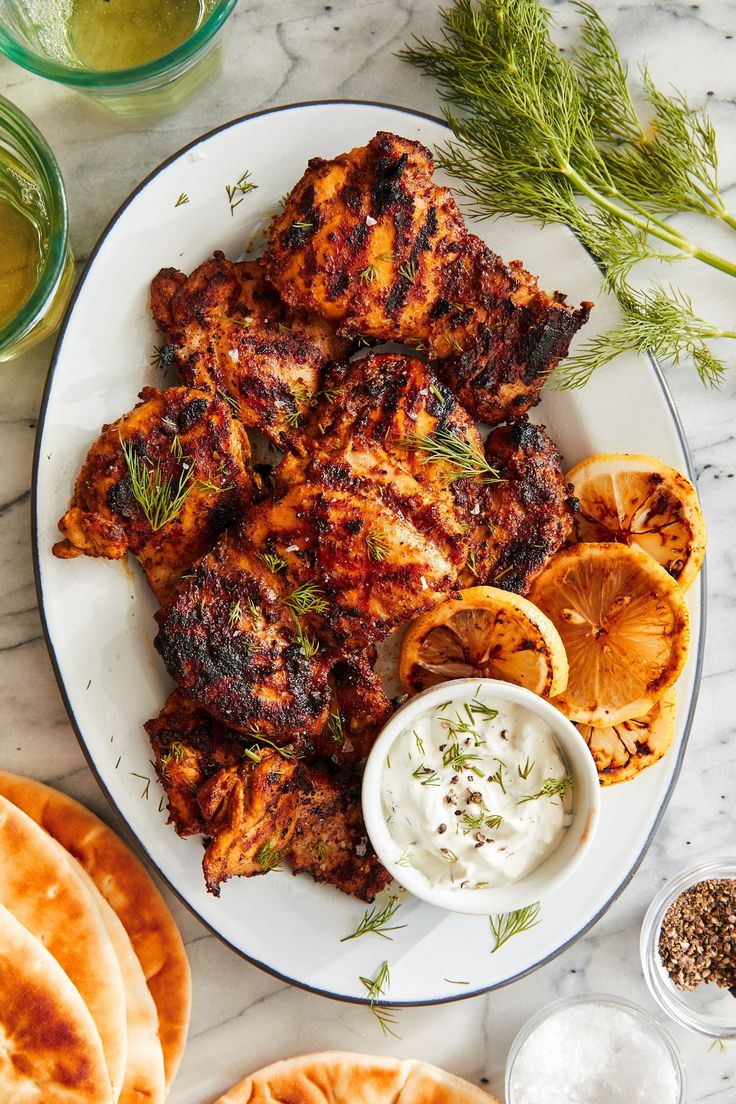 a plate with chicken wings, oranges and pita bread on it next to some dipping sauce