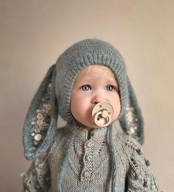 a baby doll with a pacifier in it's mouth, wearing a knitted hat and sweater