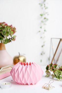 pink origami flower vase on white table next to other flowers and decor items