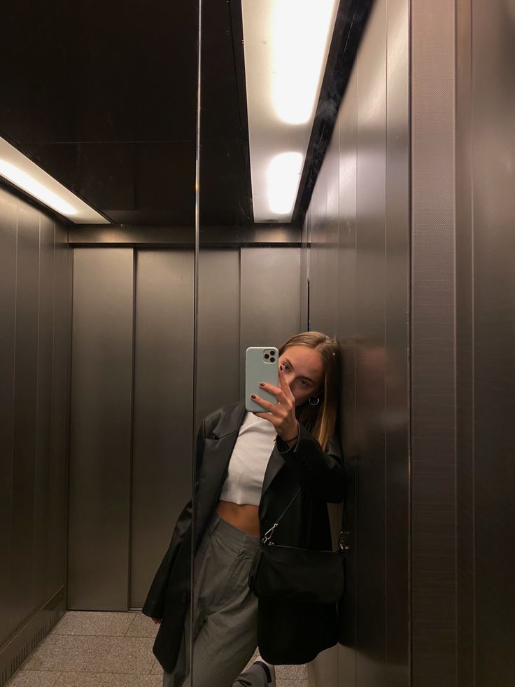 a woman taking a selfie in an elevator with her cell phone up to her ear