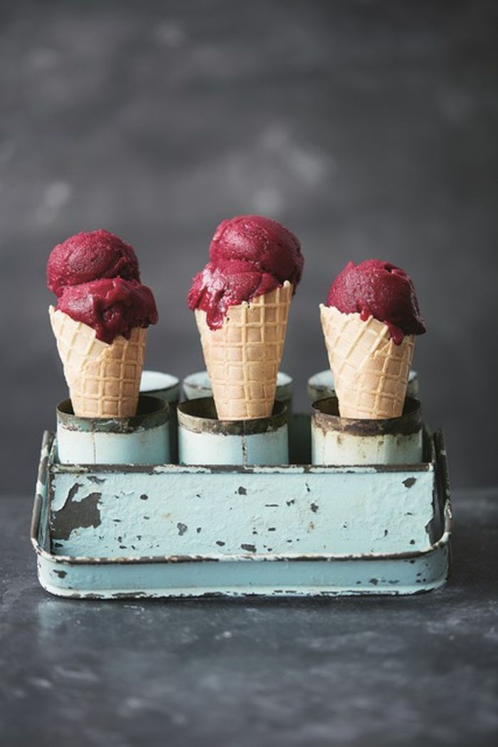 three ice cream cones sitting on top of an old blue tray filled with raspberries