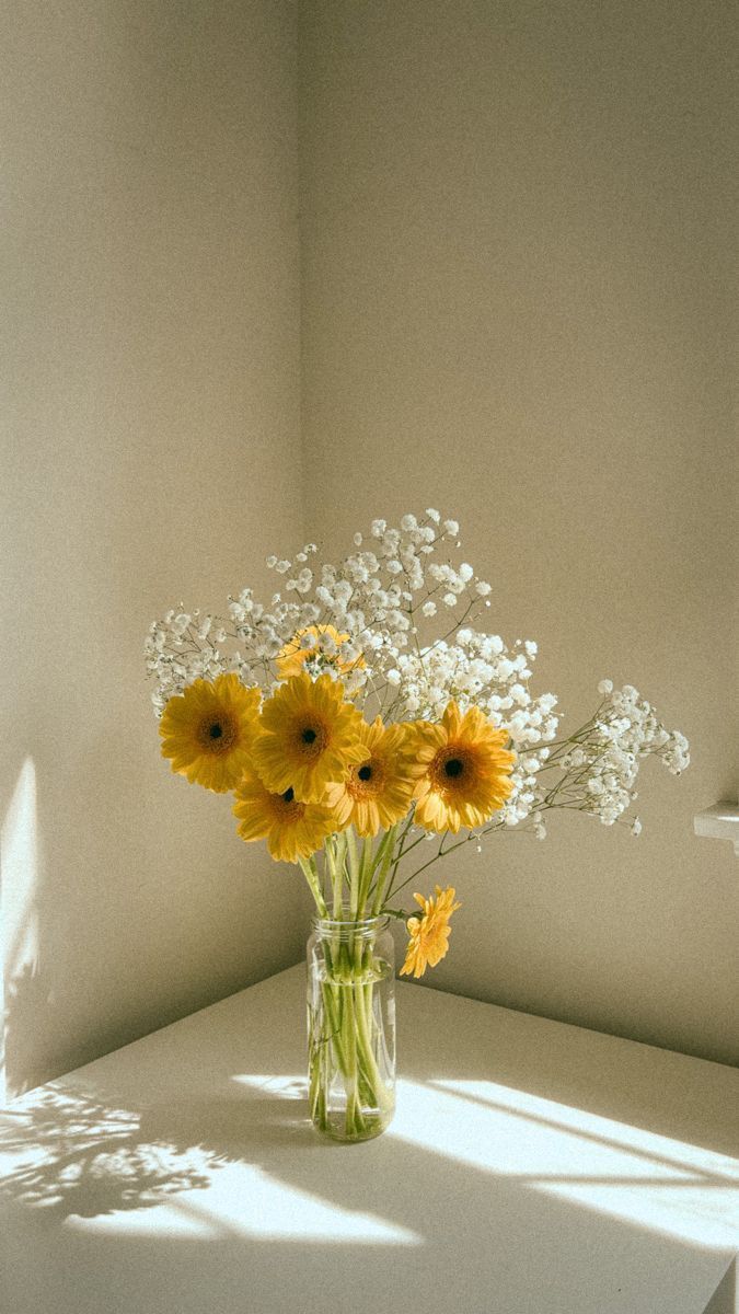 a vase filled with yellow and white flowers sitting on top of a table next to a window