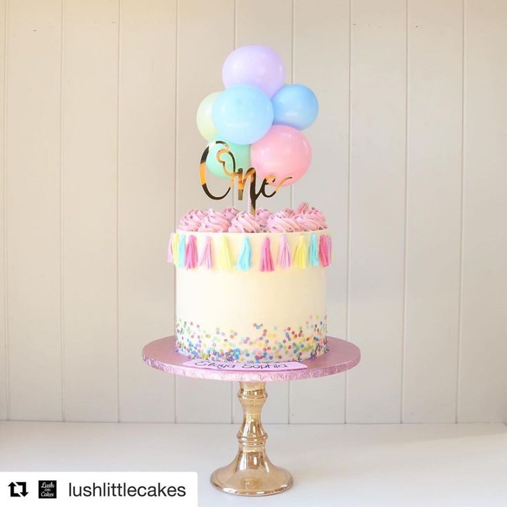 a birthday cake with balloons and the number one on top is decorated in pastel colors