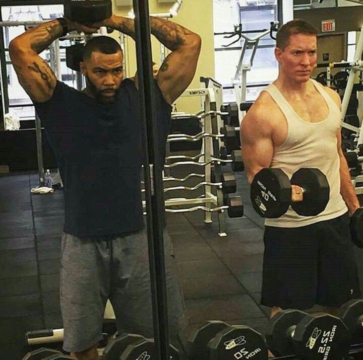 two men in a gym doing exercises with dumbbells