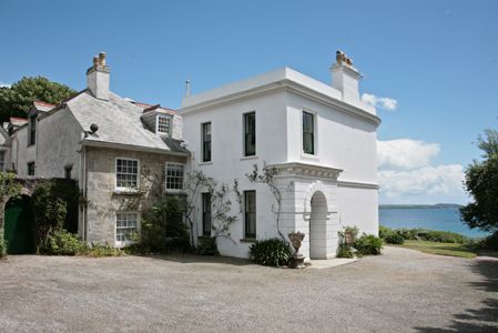 a large white house sitting on top of a lush green field next to the ocean