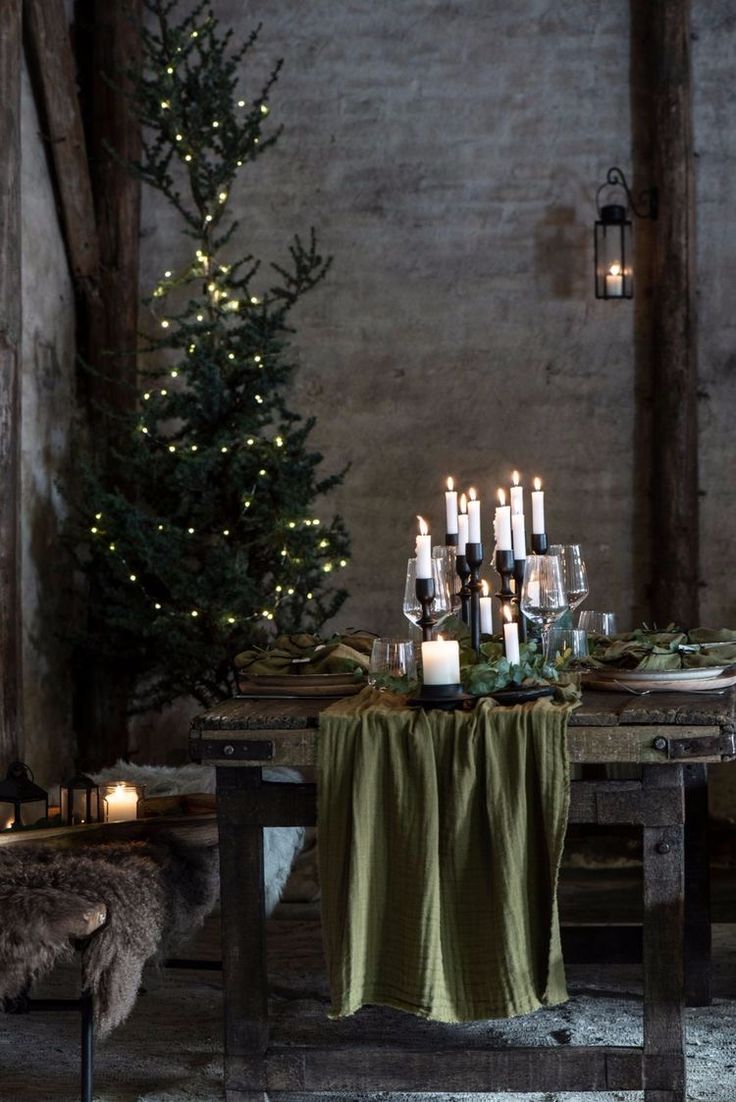 a dining table with candles and greenery on it in front of a christmas tree