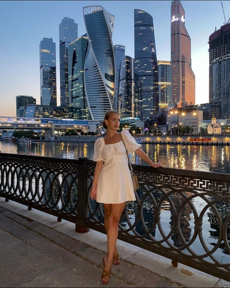 a woman is standing on a bridge in front of the cityscape at night