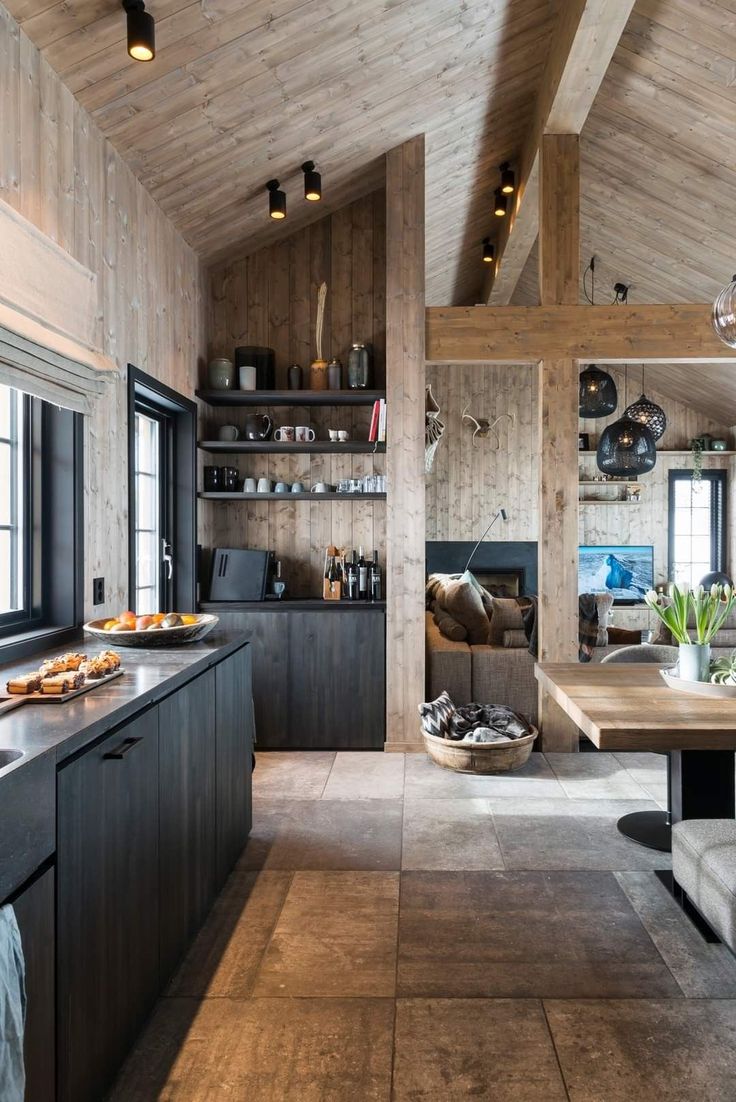 an open kitchen and dining area with wood paneling on the walls, wooden ceiling beams, and black cabinets