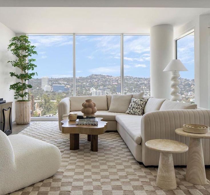 a living room filled with furniture and large windows overlooking a cityscape in the distance