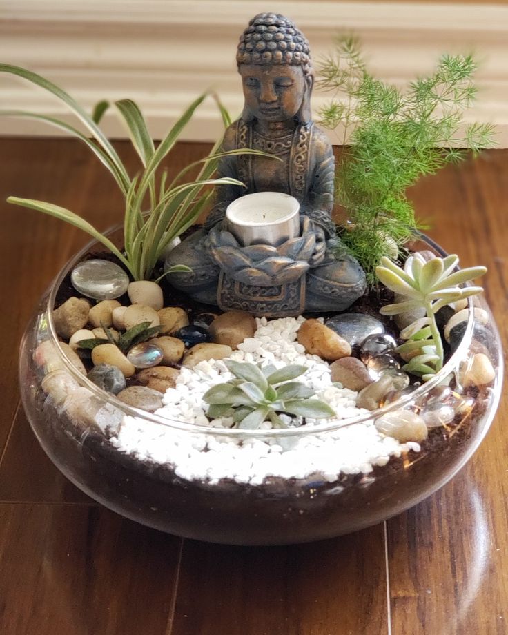 a buddha statue sitting on top of a bowl filled with rocks and succulents