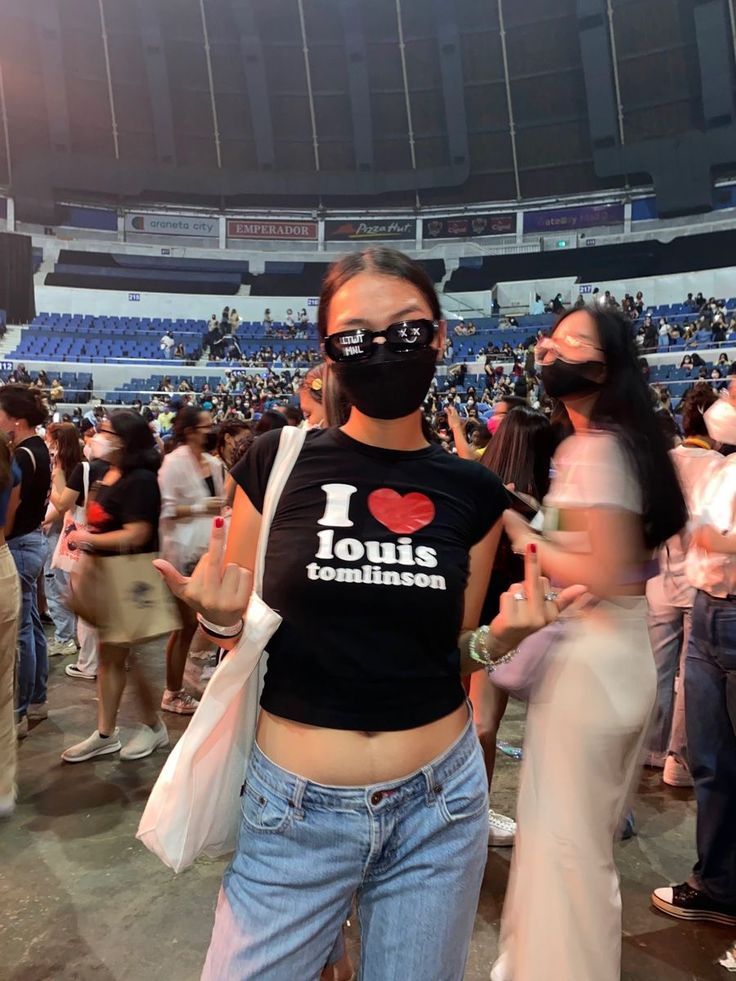 a woman wearing a face mask and jeans stands in front of an audience at a sporting event