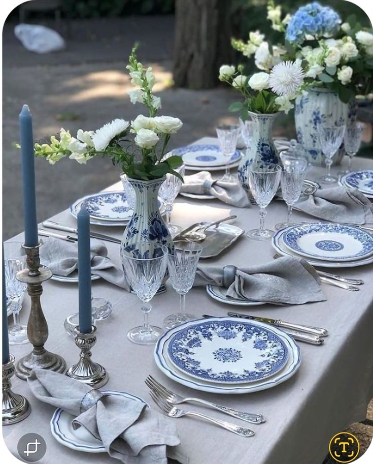 the table is set with blue and white plates, silverware, and flowers in vases