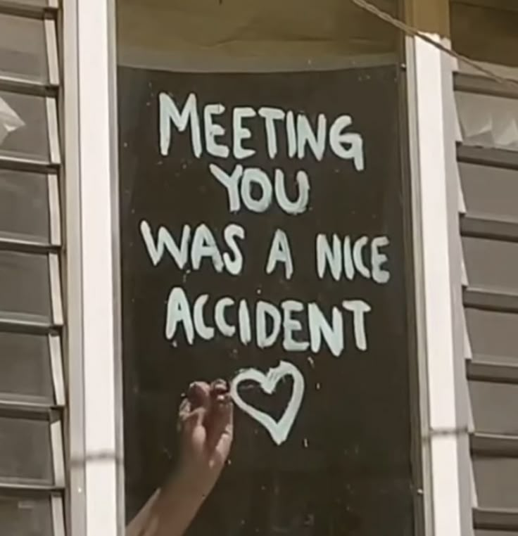 a hand writing on a sign that says meeting you was a nice accident in front of a window