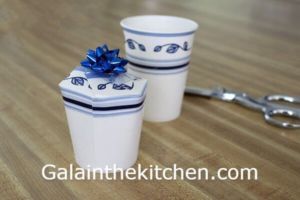 two white cups with blue bows on them sitting on a table next to a pair of scissors