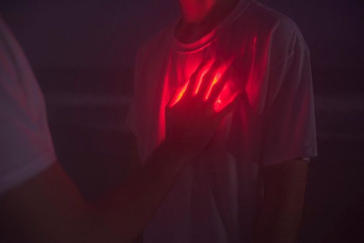 a man holding his hands up in the dark with red light shining on it's chest