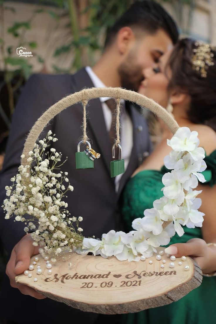 a bride and groom kissing in front of a wooden sign with flowers on it that reads,