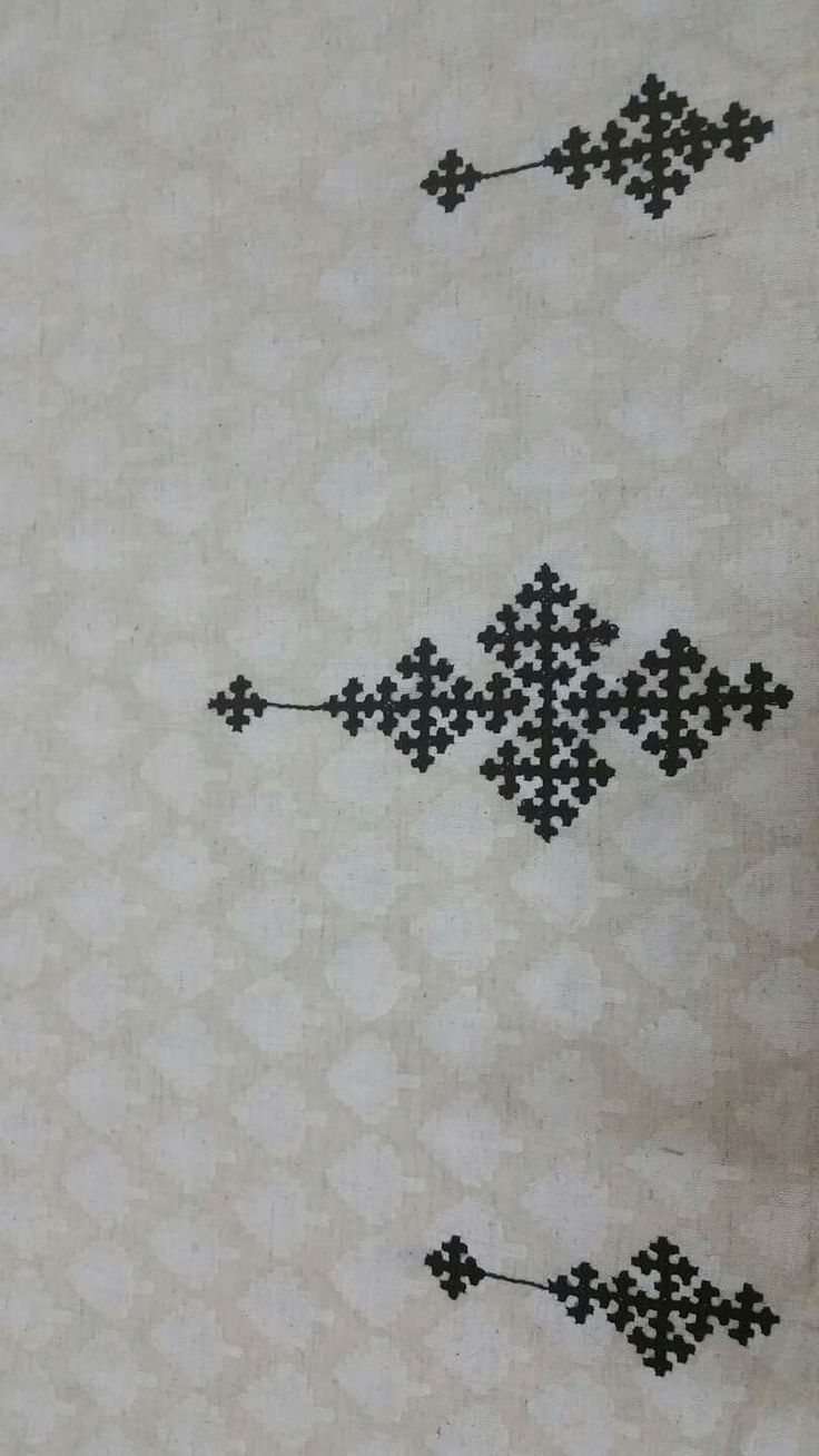 two black and white cross stitchs are on the table cloth, one has an arrow in it