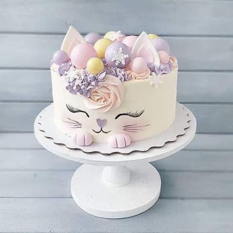 a cake decorated with pastel colored eggs and pink flowers on a white pedestal stands against a wooden background