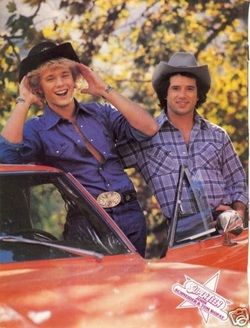 two men standing next to each other in front of a red car wearing cowboy hats