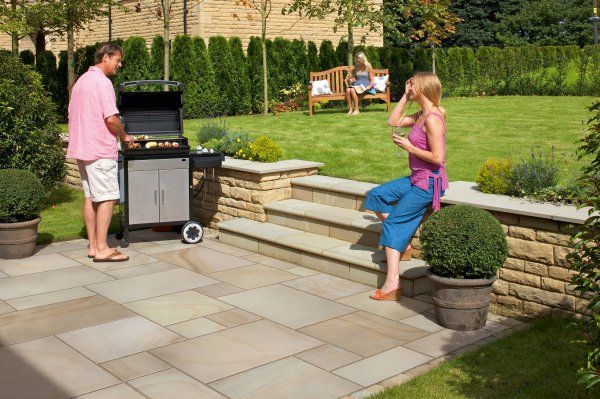 a man and woman standing in front of a bbq grill on a stone patio