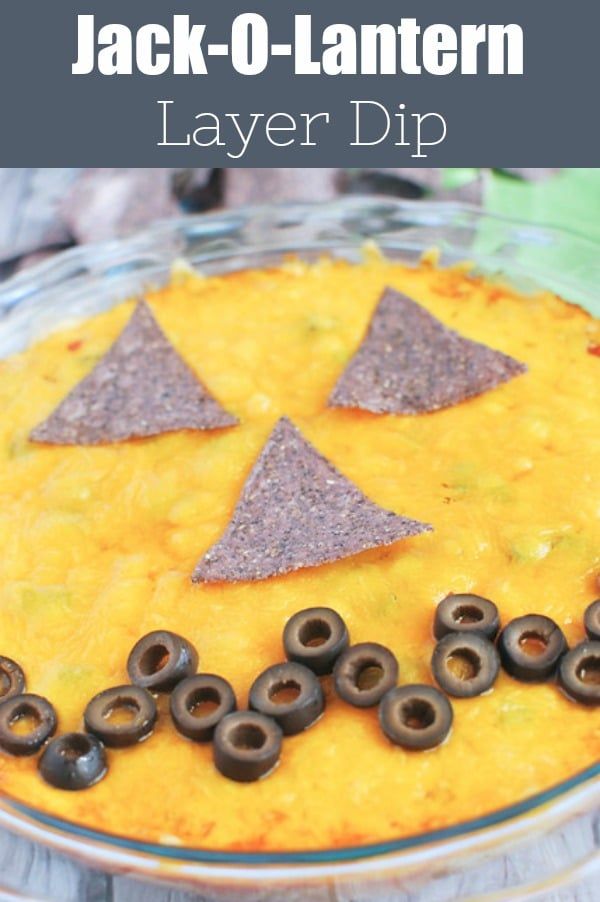 a layered dip with black olives and tortilla chips in the shape of a jack - o'- lantern