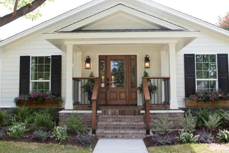 a white house with black shutters and plants on the front porch, along with steps leading up to it